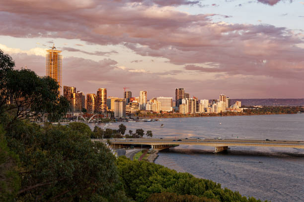 View of Perth in Western Australia, landscape with the skyscrapers, parks and bay with the bridge during sunset or sunrise. Clouds on the dramatic blue sky.