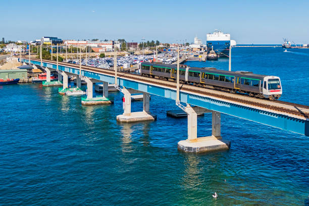 Nature and Industry: aerial view electric commuter train crossing Swan River bridge with Fremantle Port Inner Harbour activity in background and pelican in foreground.