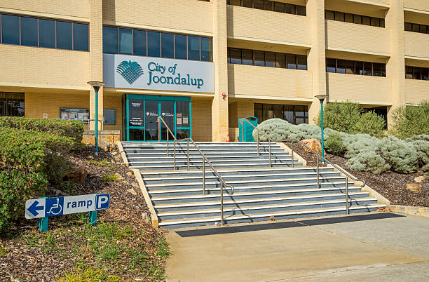 Exterior view of a public building with stairs leading to the glass doors, accompanied by a clear accessibility sign