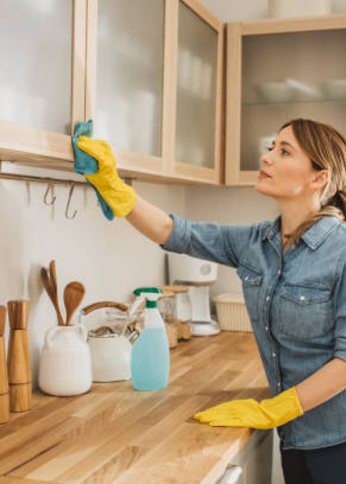 Young woman using detergent or disinfectant to wash and wipe a surface at kitchen.
