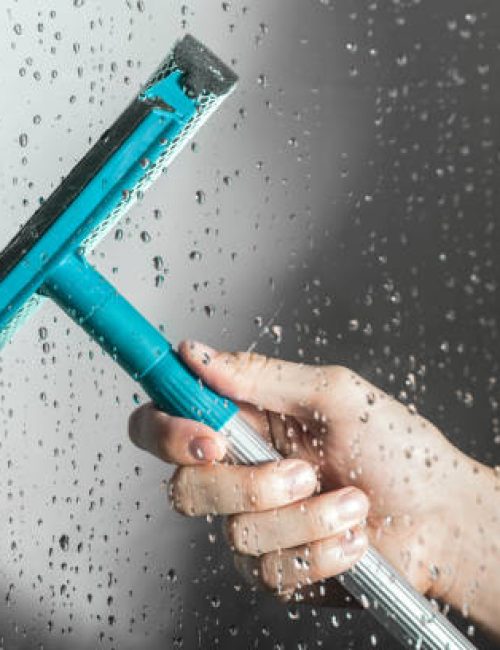 close up cleaning shower glass door with squeegee