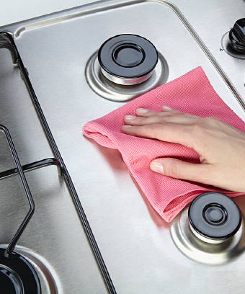 The woman cleaning set-top stove with rag