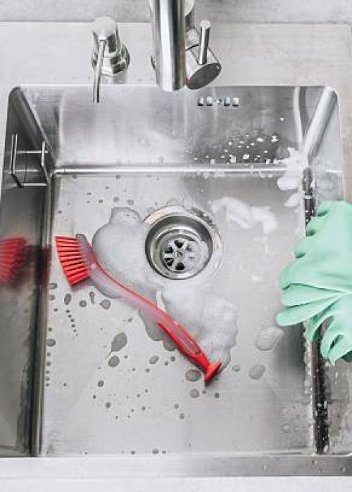 Cleaning Supplies and Soap Bubbles in a Kitchen Sink with Metallic Finish and Gloves