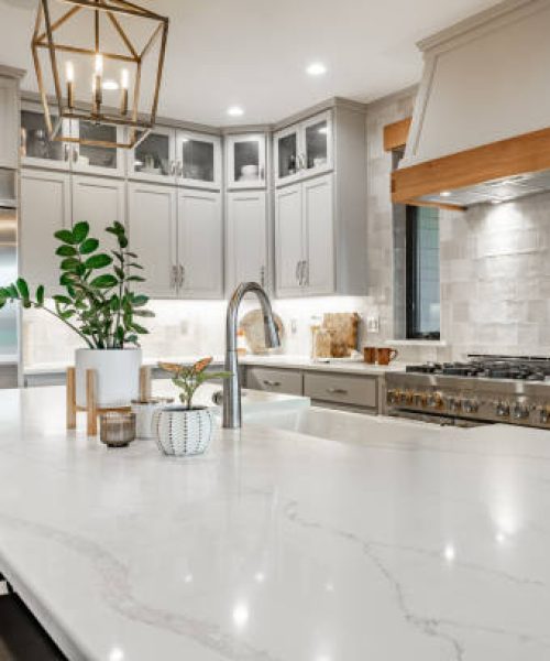 Large kithchen with white countertops, grey cabinets, stainless appliances, large white porcelain double sink farmhouse style.