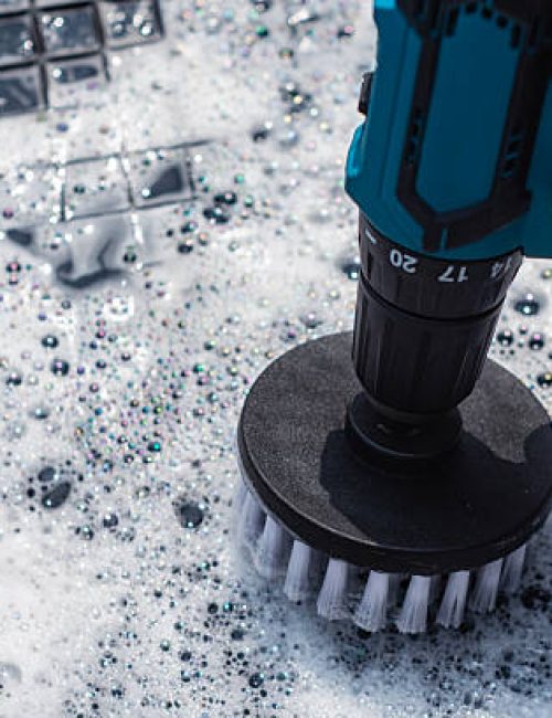 Close-up of an electric drill with a brush like attachment for cleaning a car rubber mat with soapy foam. Cleaning and hygiene concept