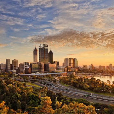 Gold warm sun light litting CBD of Perth city as seen from Kings park with green trees and highway entering the city.