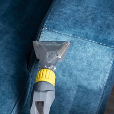 A steam cleaner is being used on a blue upholstered sofa, effectively removing dirt and stains. The modern living room provides a cozy atmosphere with natural light.
